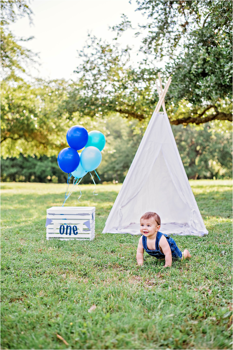 First Birthday Photoshoot of Little Boy wearing overalls with blue balloons and teepee Child Photographer Natural Light Photography Round Rock Texas