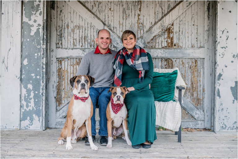 Couple with two boxers outside of barn during Christmas Mini photoshoot in Georgetown Texas by natural light portrait photographer